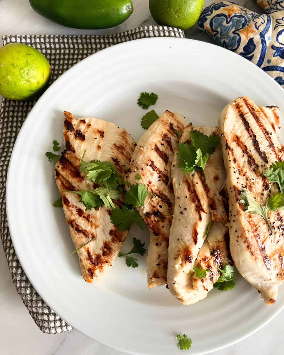 Tequila lime chicken on a white plate garnished with cilantro next to a lime. 