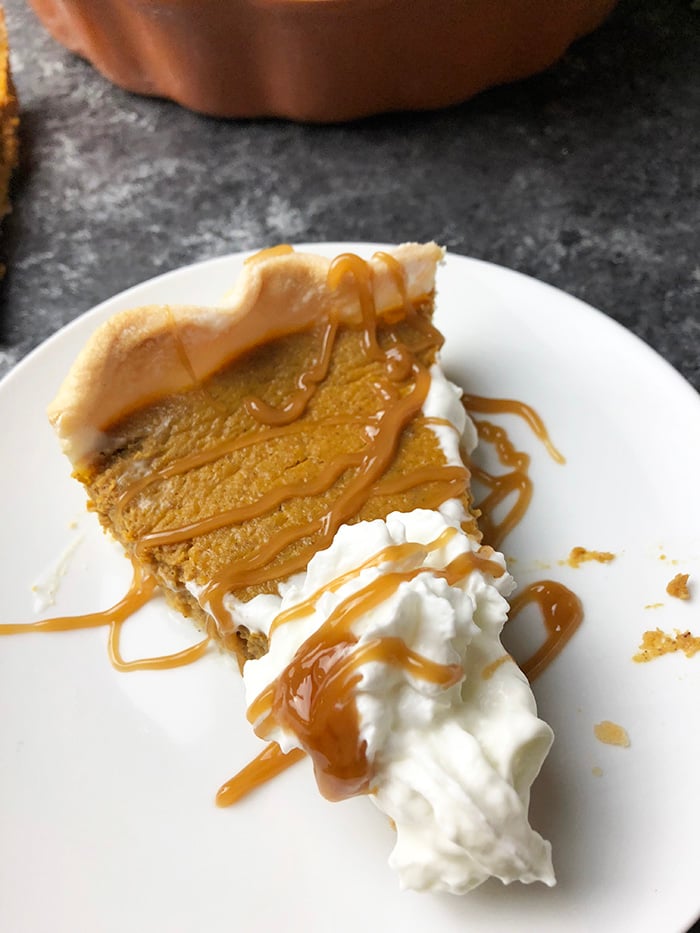 Pumpkin pie topped with whipped topping and drizzled with caramel sauce.