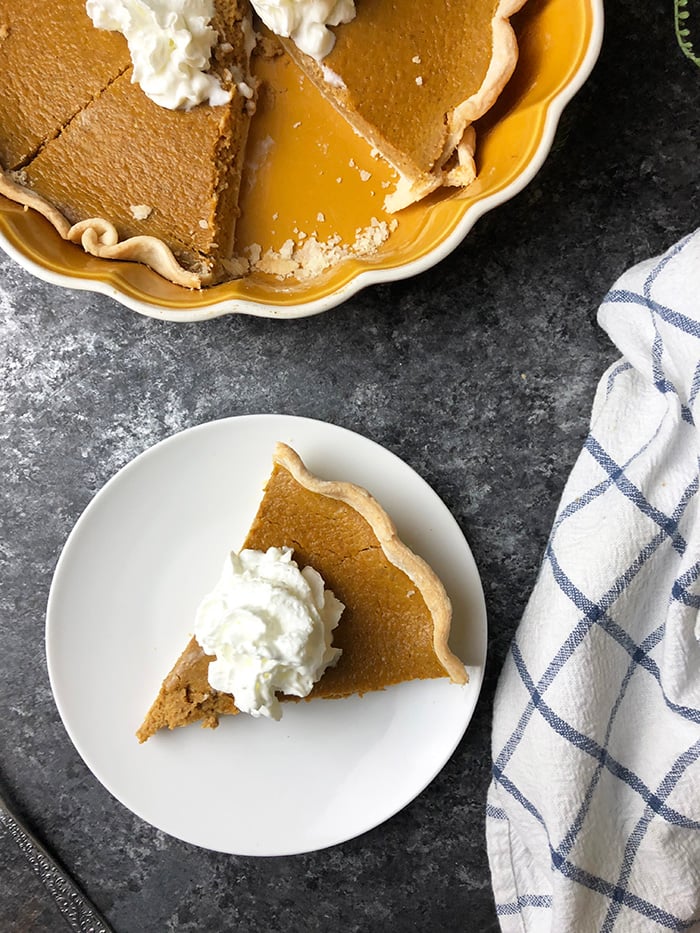 Pumpkin pie topped with whipped topping served in a pie dish.