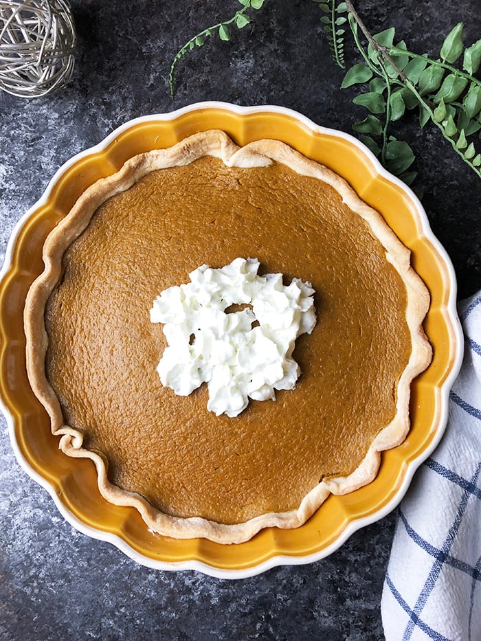 Pumpkin pie topped with whipped topping served in a pie dish. 