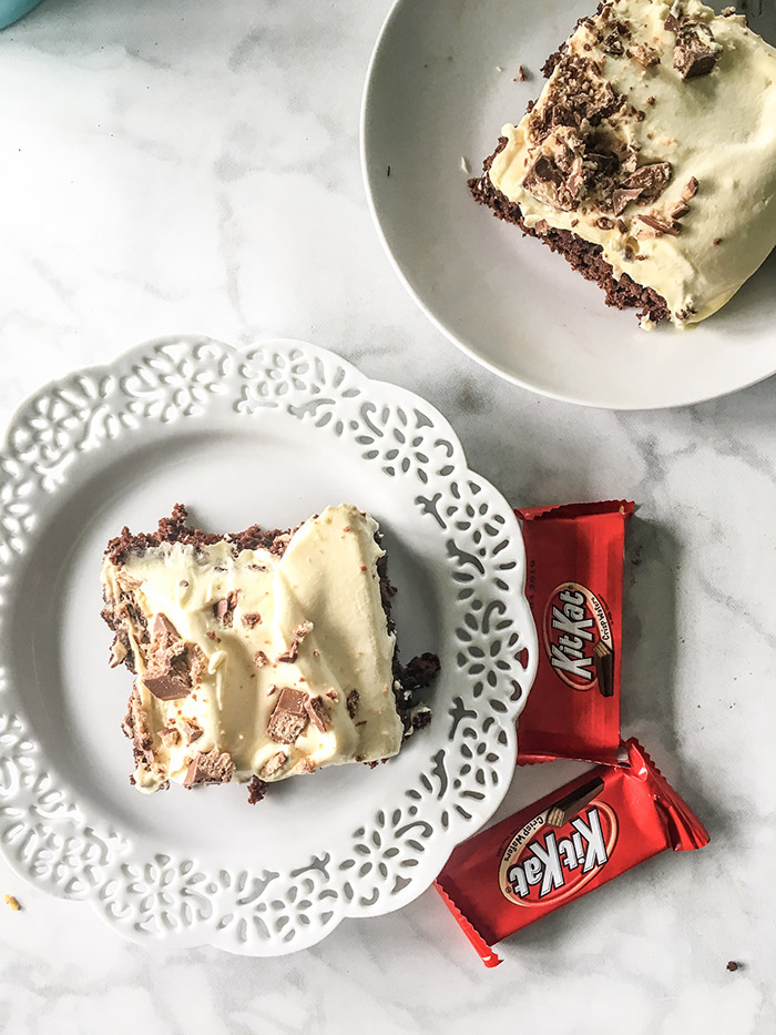 chocolate cake mix topped with vanilla pudding frosting and chopped up kit kats on a white plate. 