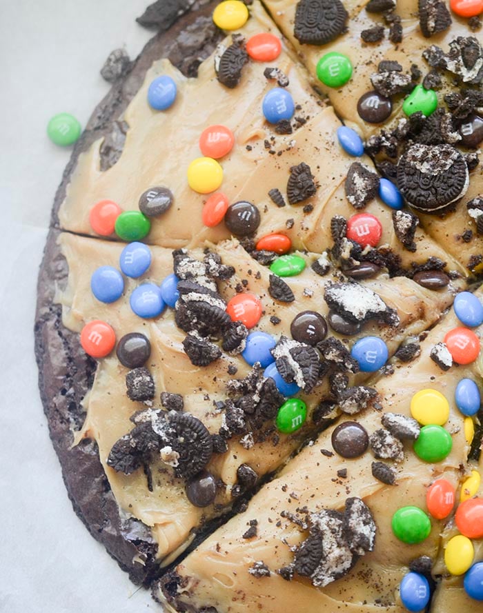 Brownie pizza topped with peanut butter frosting, crushed Oreos, M&M's, and candy pieces. 