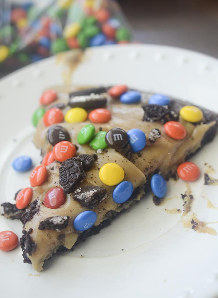 Brownie pizza topped with peanut butter frosting, crushed Oreos, M&M's, and candy pieces. 