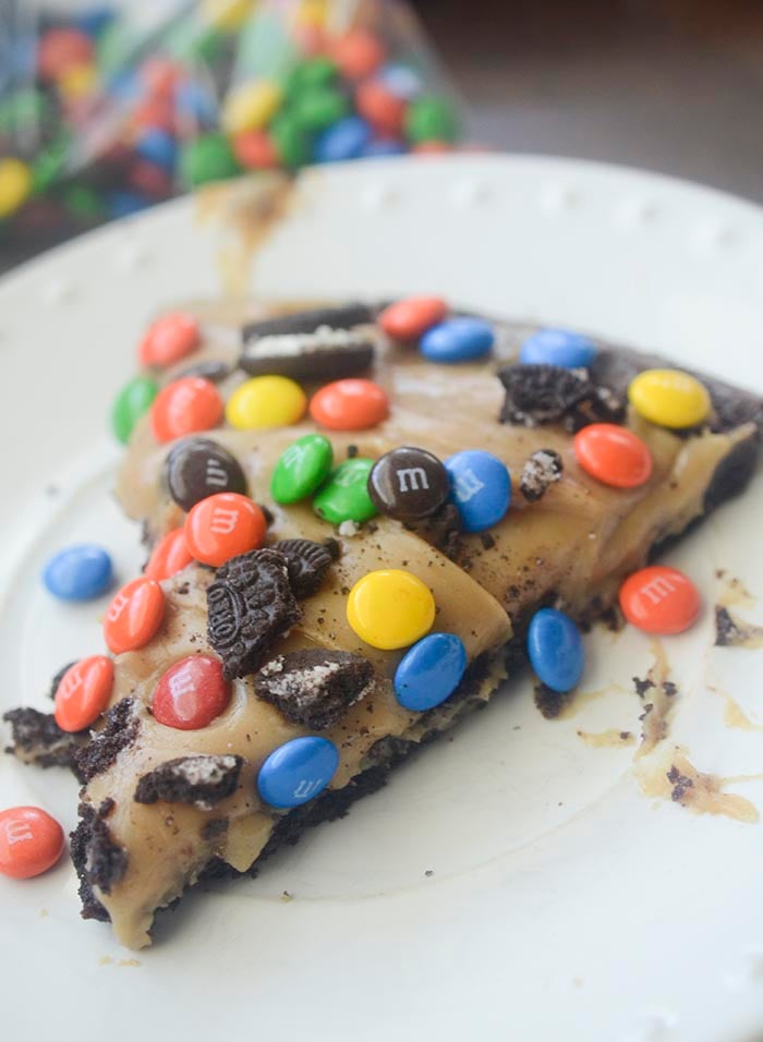 Brownie pizza topped with peanut butter frosting, crushed Oreos, M&M's, and candy pieces.