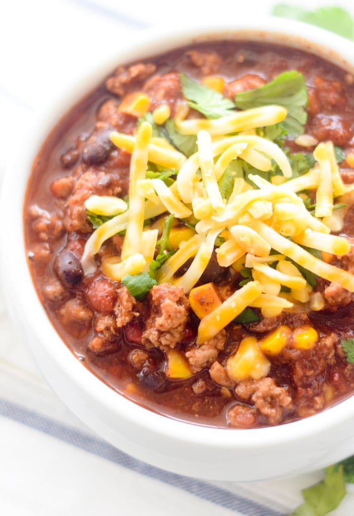 Turkey, Corn, and Black Bean Chili topped with cheese and fresh parsley in a white bowl. 