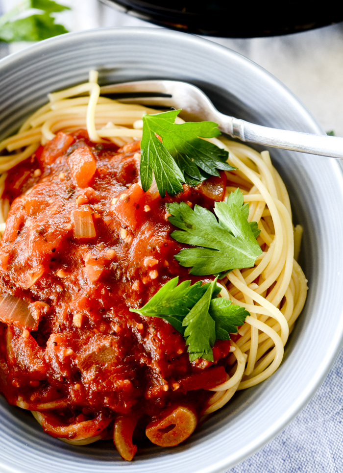 Marinara sauce with spaghetti noodles in a bowl topped with parsley. 