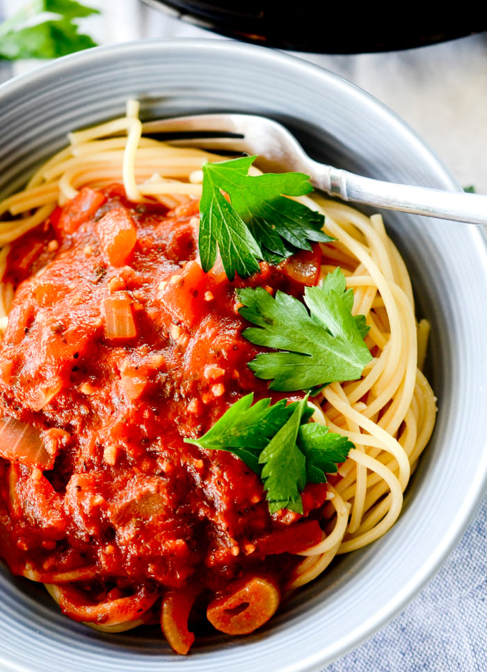 Marinara sauce with spaghetti noodles in a bowl topped with parsley. 