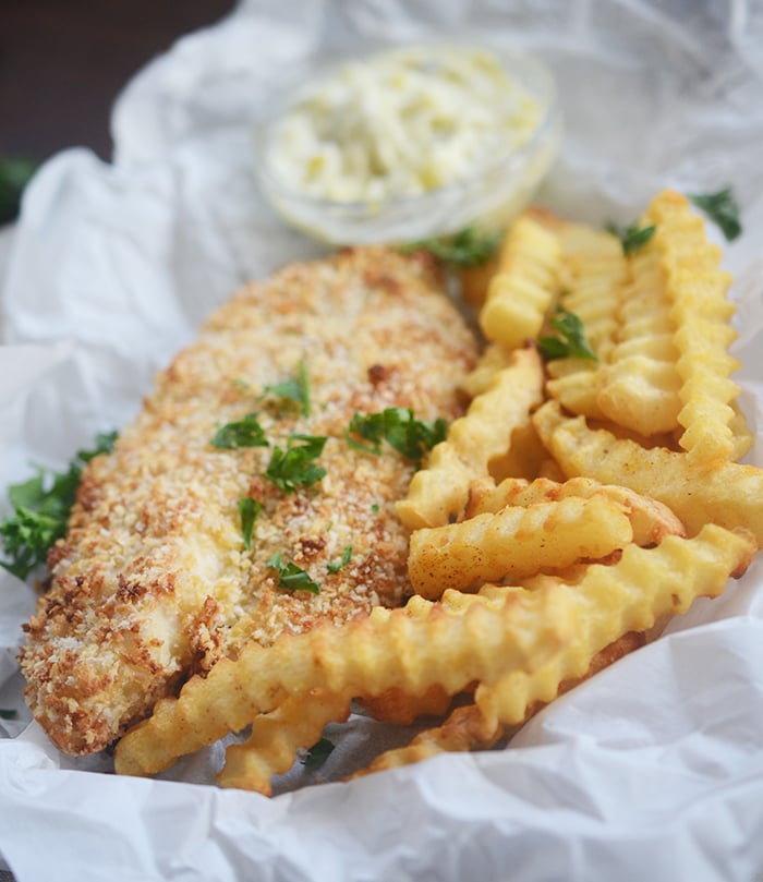 Air fryer fried breaded fish with french fries on some parchment paper garnished with parsley.