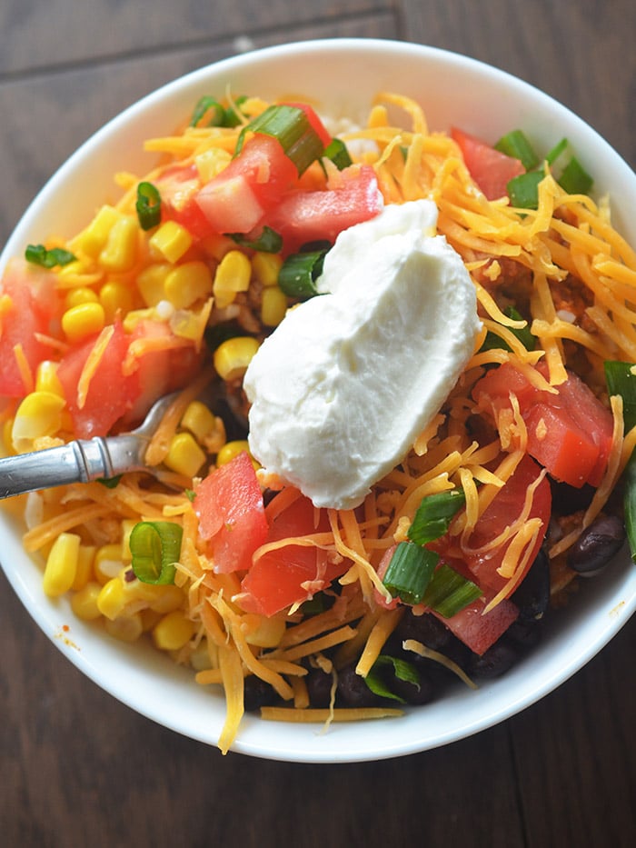 Burrito bowl topped with yogurt and all the fixings in a white bowl 