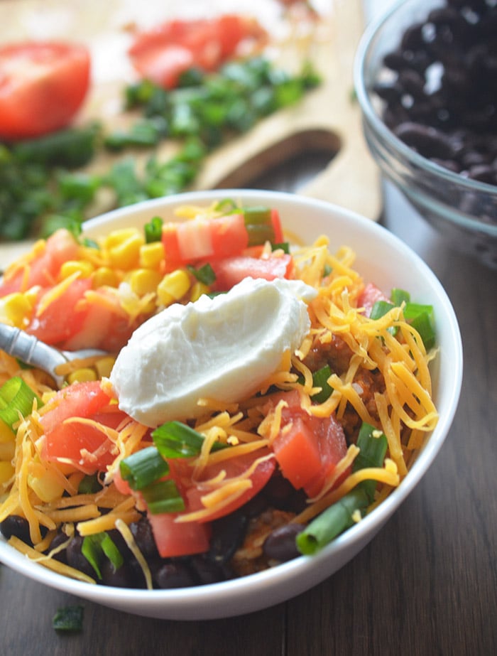 Burrito bowl topped with yogurt and all the fixings in a white bowl 