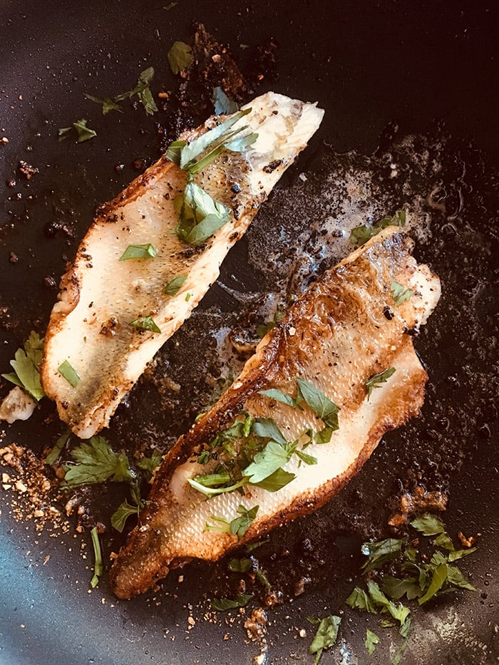 pan seared walleye in a skillet topped with fresh parsley.
