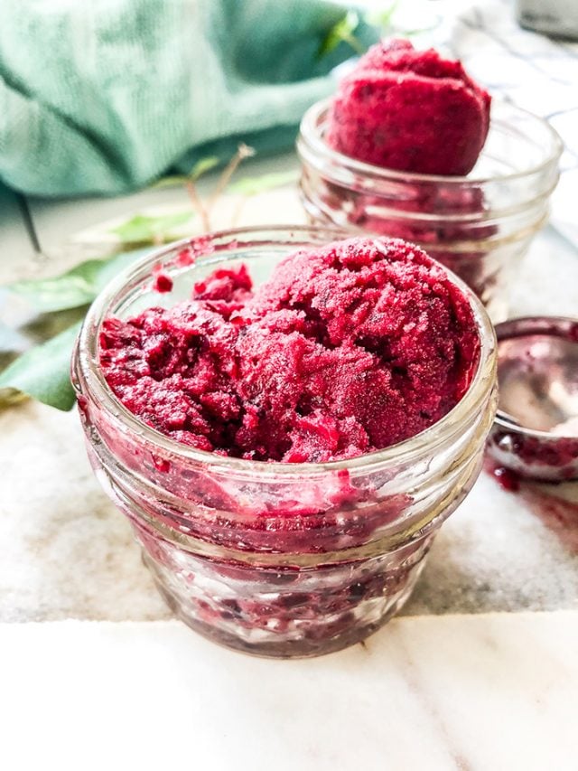 Cherry sorbet in glass jars next to a blue napkin. 