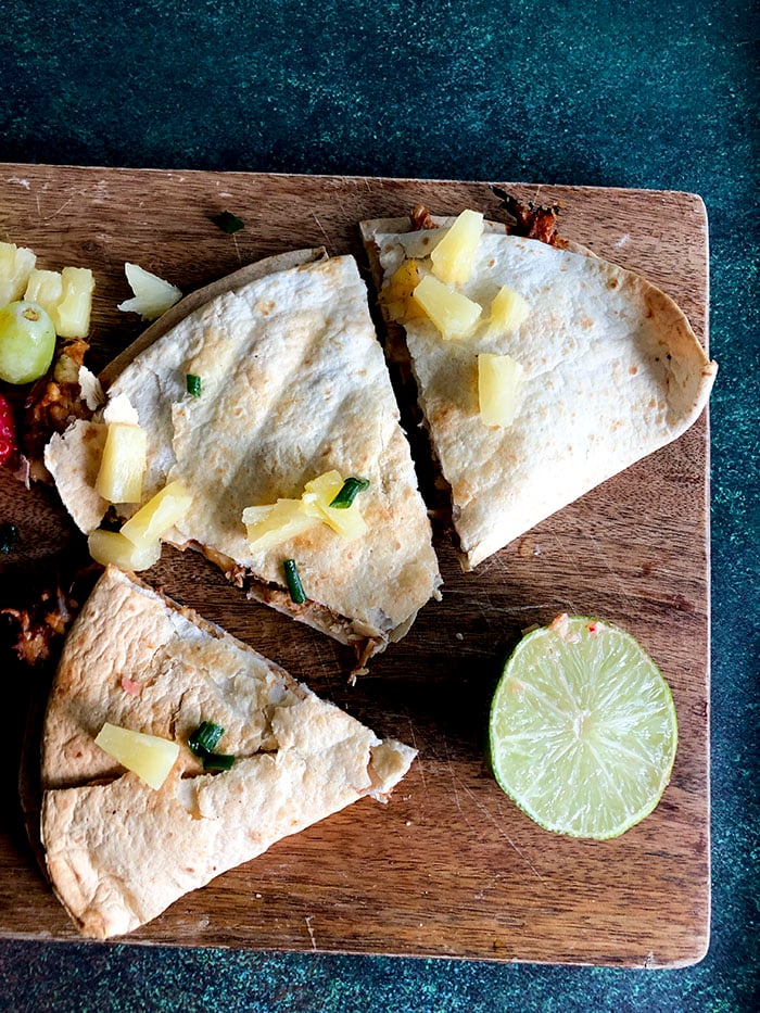 Air fried Chicken quesadillas on a wooden cutting board next to a lime wedge. 