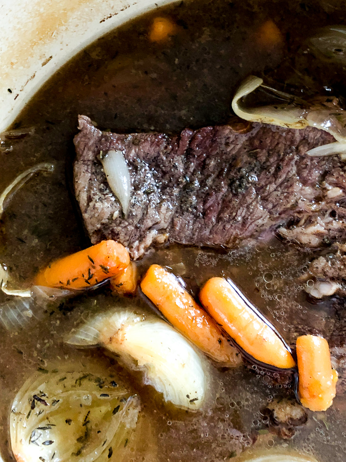 Pot roast cooking in a pan with onions and carrots. 