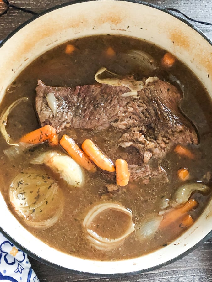 Pot roast cooking in a pan with onions and carrots. 