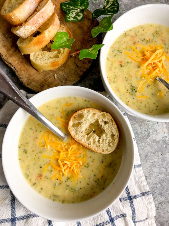 Broccoli cheddar soup topped with cheese and a baguette slice in a white bowl. 