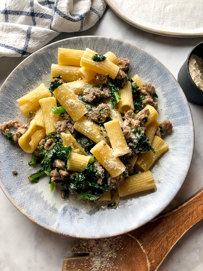 Rigatoni with Sausage and Kale  on a blue plate topped with parmesan cheese. 
