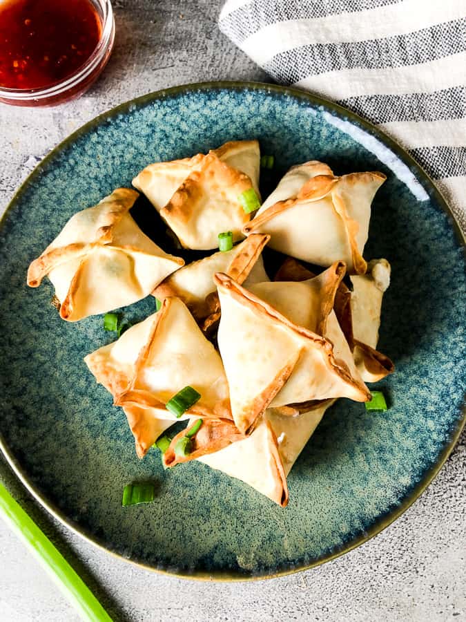 Crab rangoons on a blue plate garnished with green onions. 