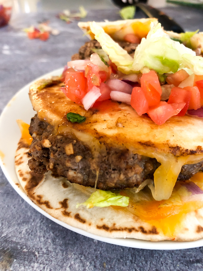 Quesadilla Burger between two street tacoo shells and topped with pico de gallo 