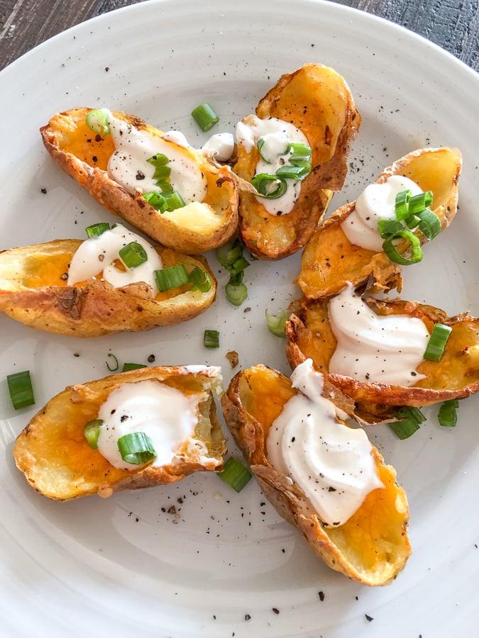 Air fryer potato skins on a white plate garnished with green onions. 