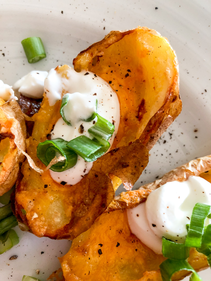Air fryer potato skins on a white plate garnished with green onions. 