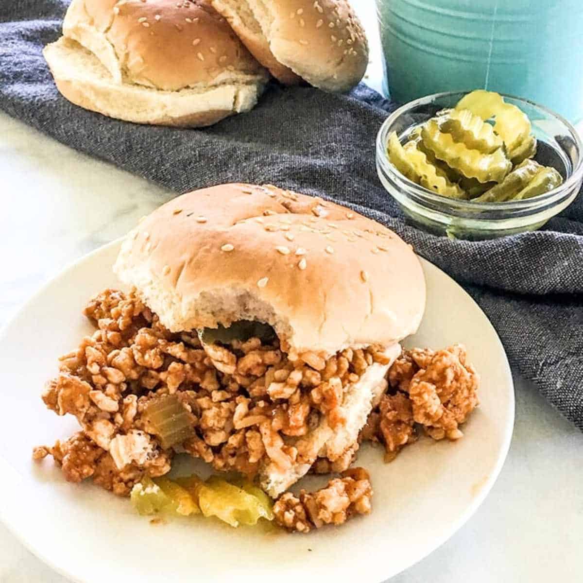 Sloppy joes served on a bun on top of a white plate.