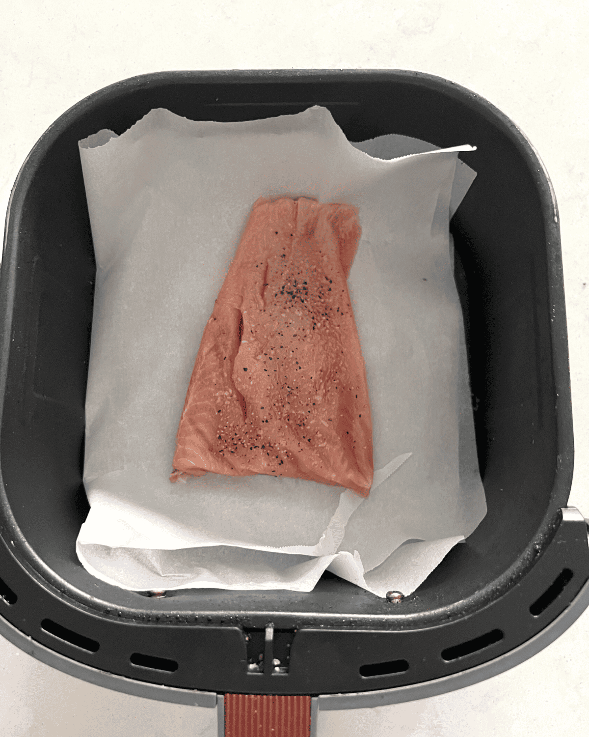 seasoned salmon filet in an air fryer basket with parchment paper.