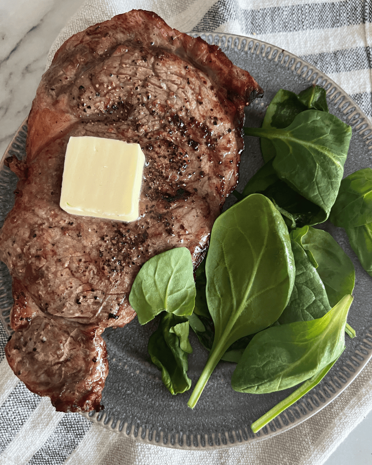 seasoned air fryer steak on a grey plate with some fresh spinach. 