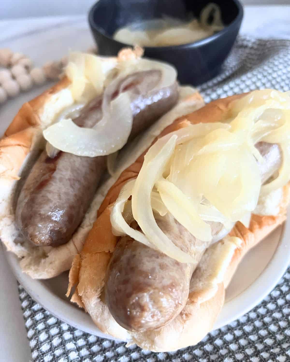 Grilled beer brats in a soft hot dog bun topped with soft onions. 