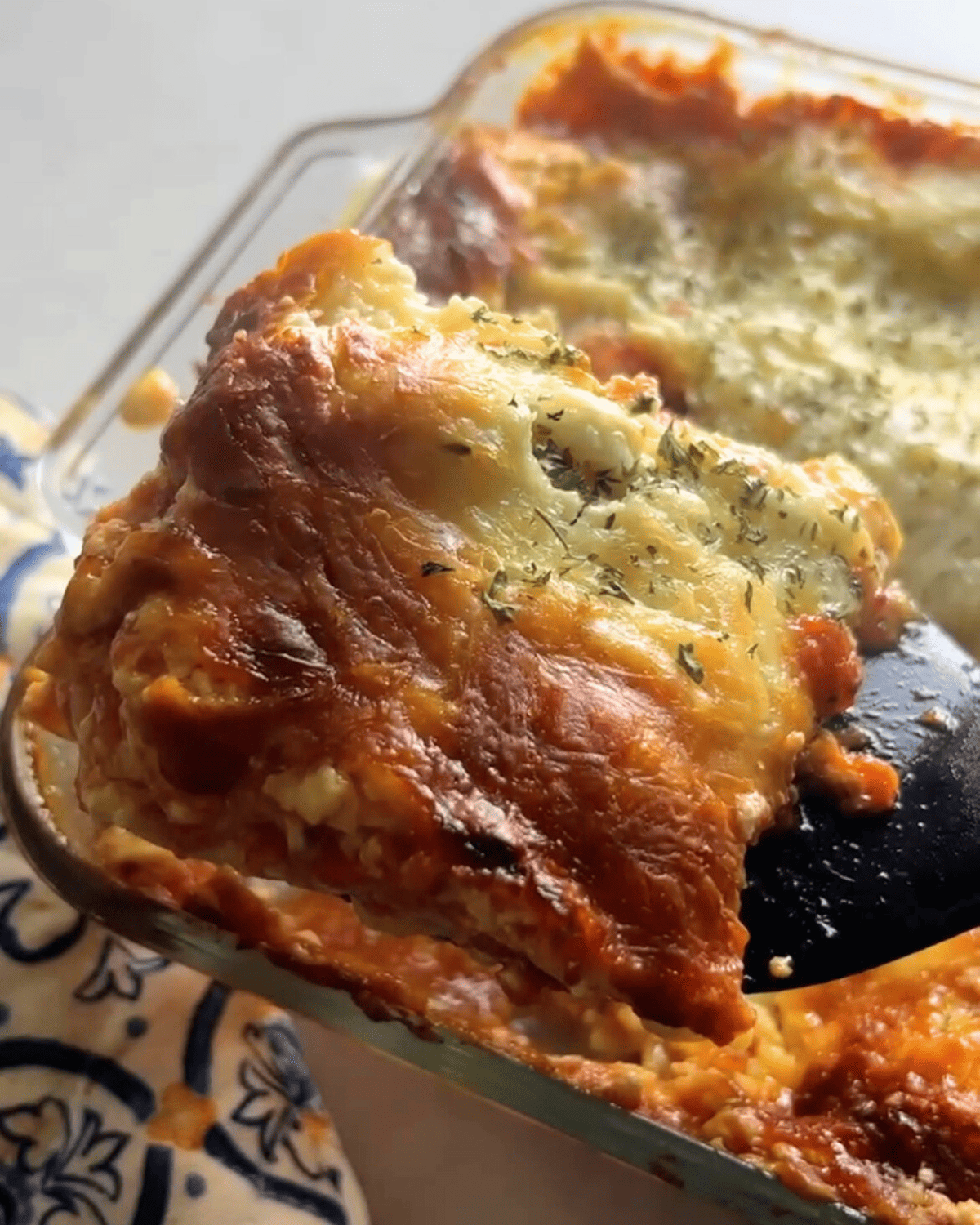 Finished buffalo chicken lasagna in a baking dish being served with a utensil 