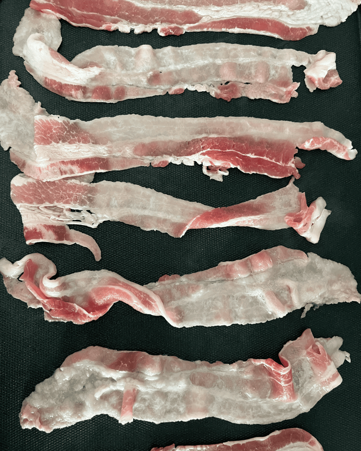 uncooked slices of bacon strips on a blackstone griddle. 