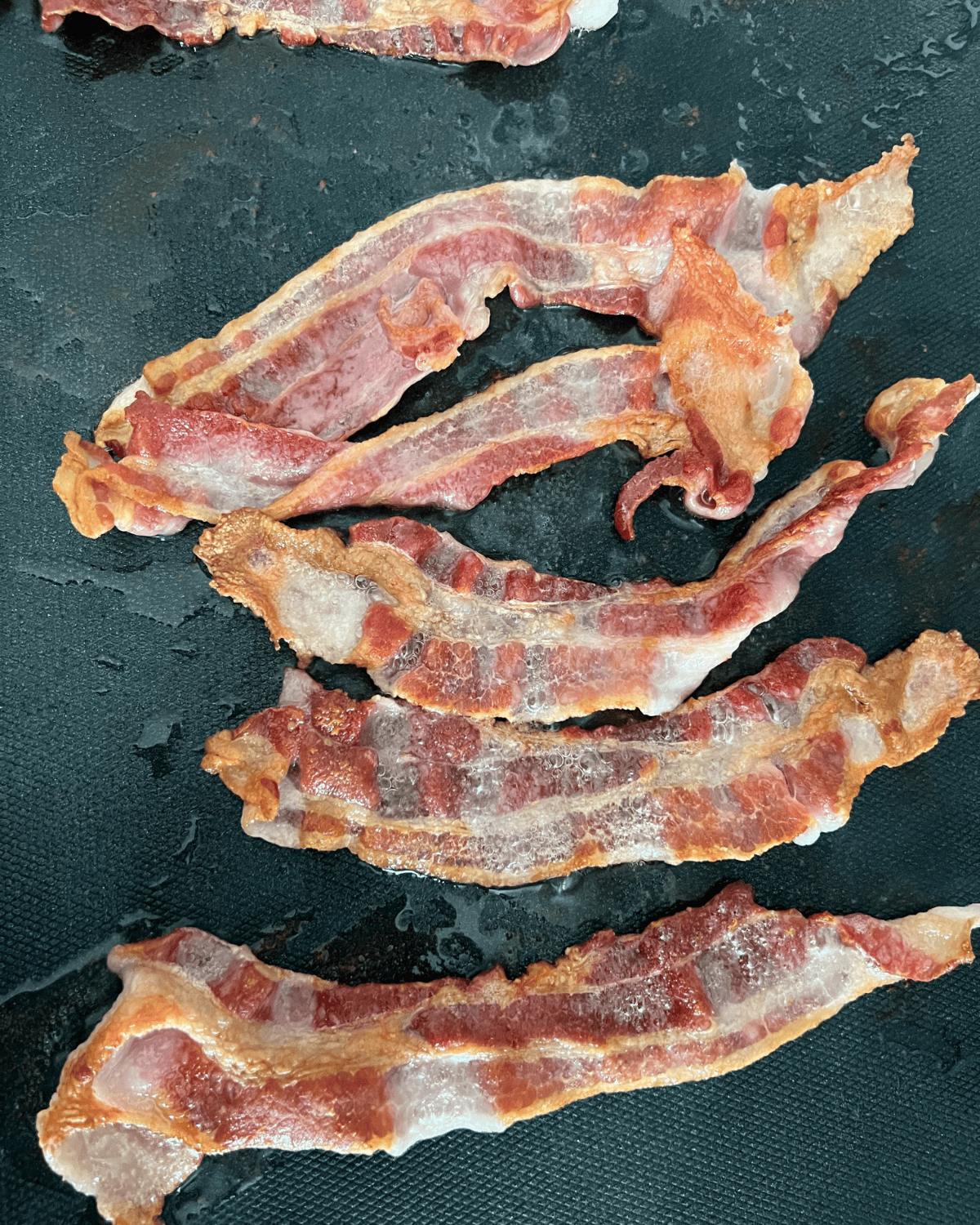 cooked slices of bacon strips on a blackstone griddle. 
