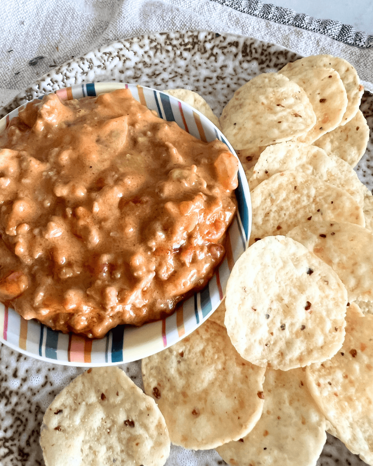 smoked queso dip in a bowl next to chips on a speckled pottery plate 
