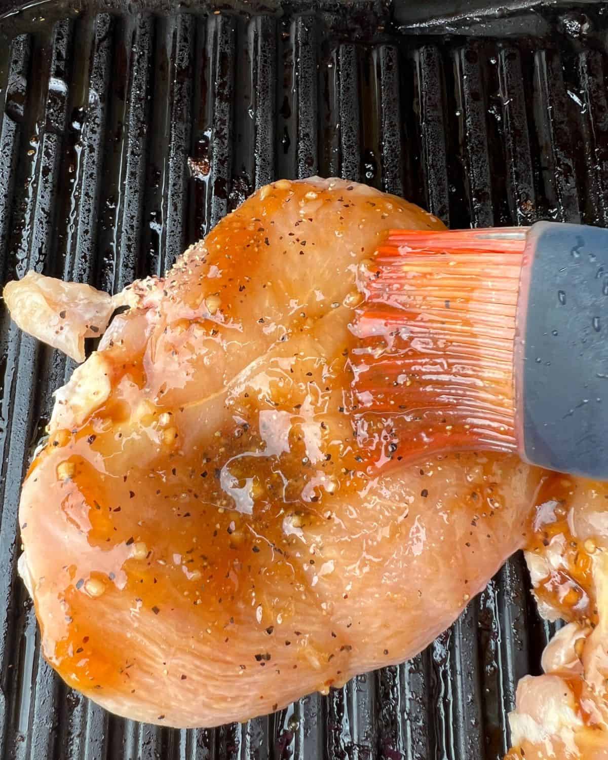 Peach glaze brushed on a chicken breast that is cooked on a grill. 