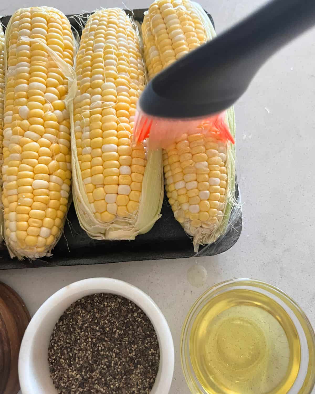 Brushing oil on fresh corn on the cob. 