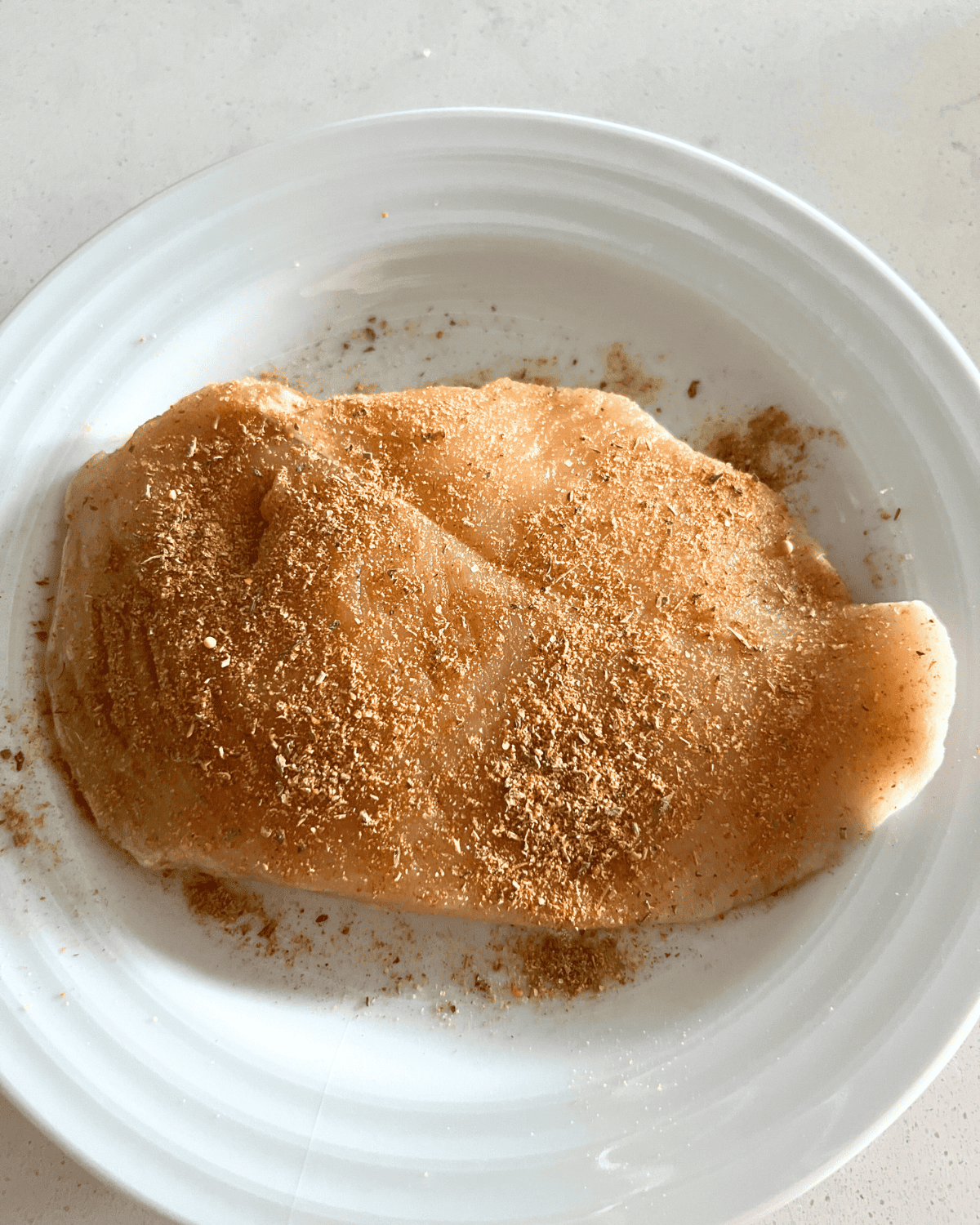 seasoned chicken breast ready for air fryer on a white plate 