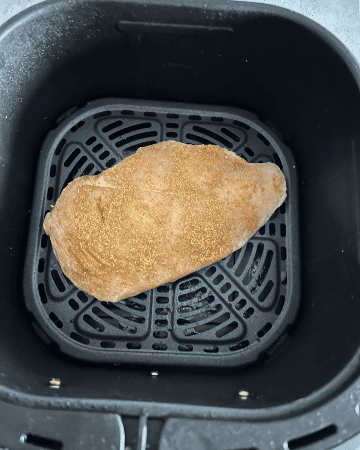 seasoned chicken breast in air fryer basket before cooking 