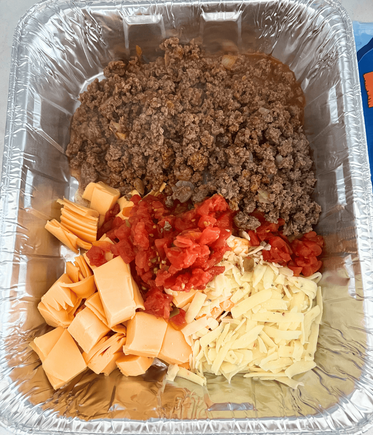 Smoked queso dip ingredients together in aluminum pan 