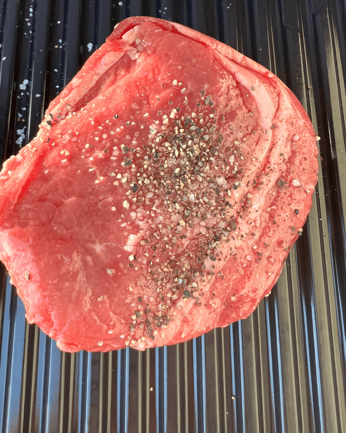 Seasoned steak placed on grill grates. 