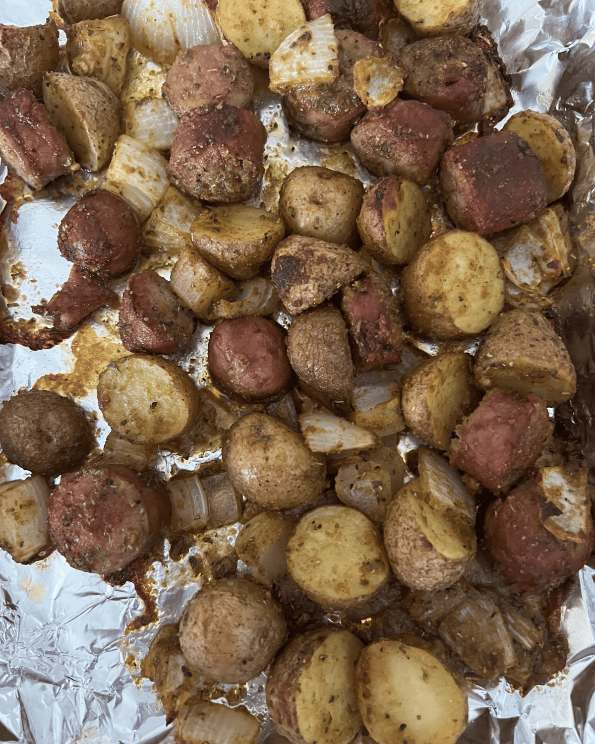 completed oven roasted smoked sausage, potatoes, and onion, on a lined foil sheet.