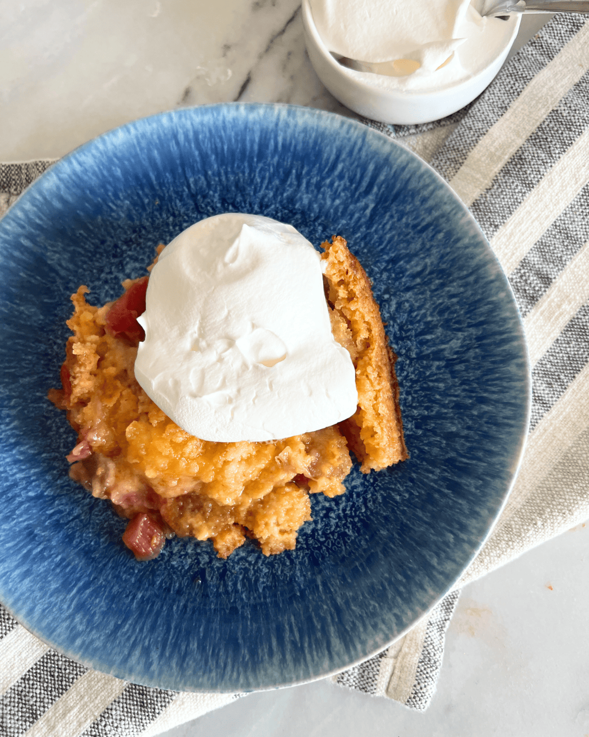 Finished rhubarb dump cake on a blue plate with a dollop of whipped topping. 