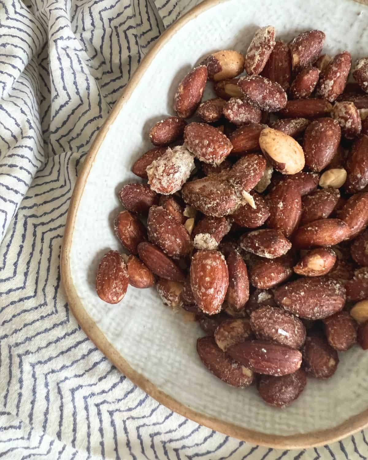 Seasoned flavorful smoked almonds in a white dish on a patterned napkin. 