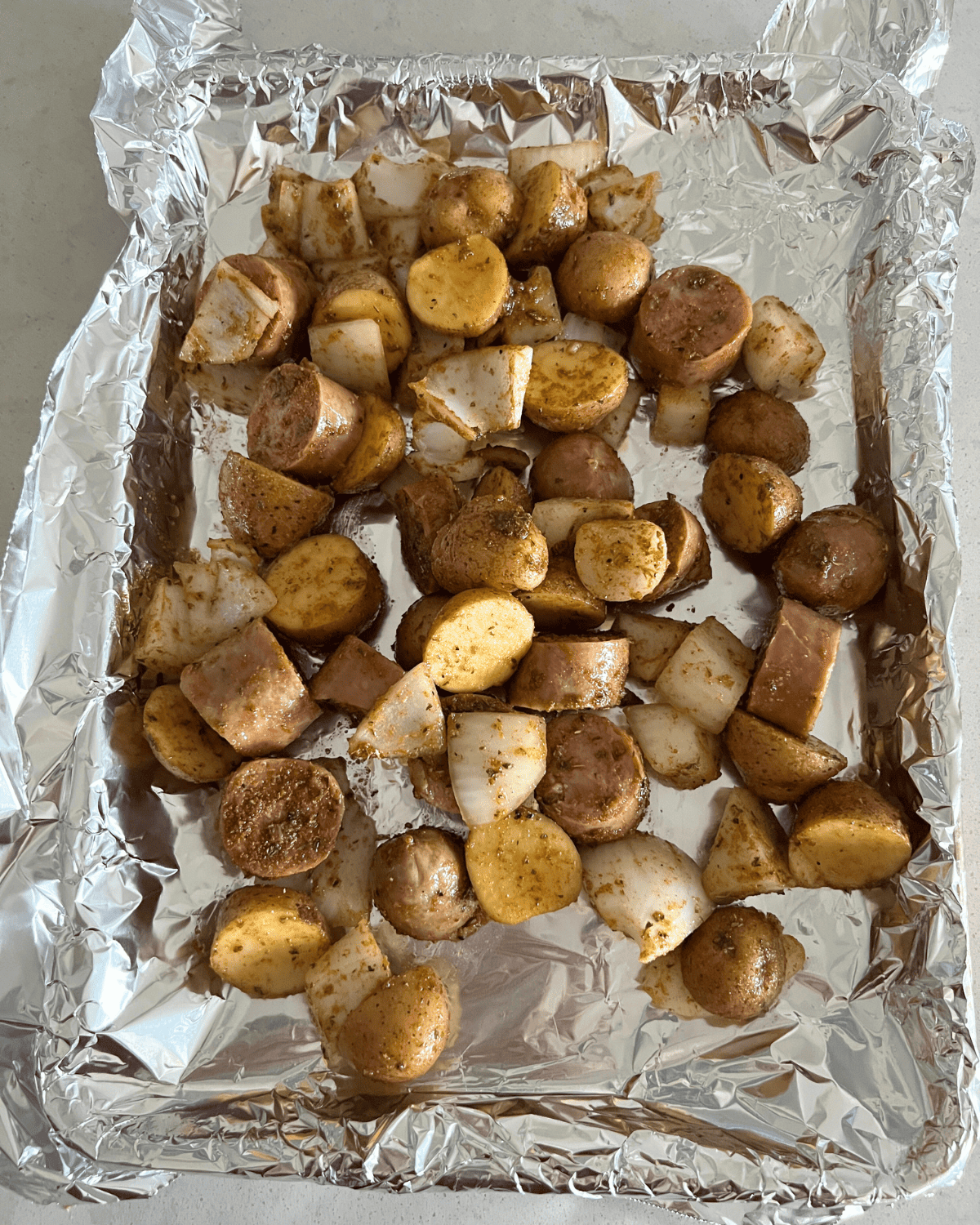 seasoned potatoes, onions, and sausage on a lined foil sheet pan. 