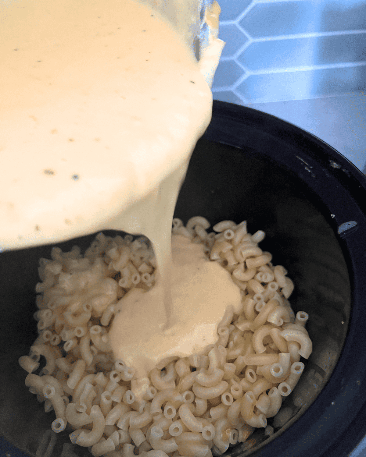 cheese sauce being poured into slow cooker over noodles.