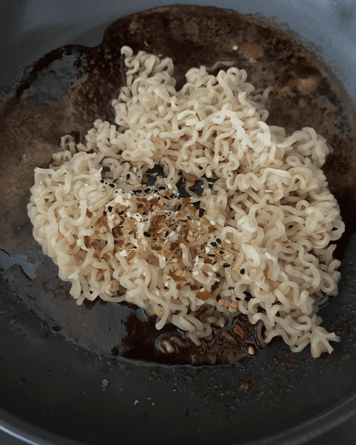 bagel seasoning and crushed pepper flakes on top of ramen noodles in a skillet 