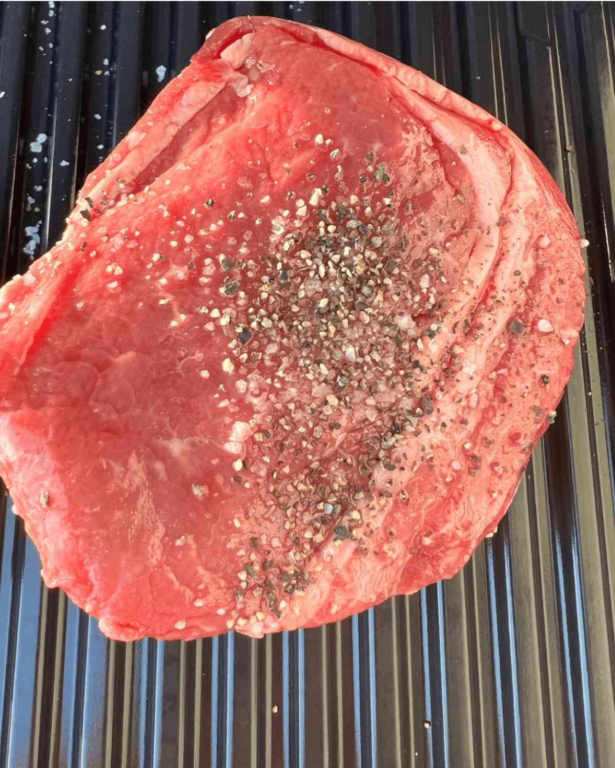 Top sirloin steak seasoned on a grill. 
