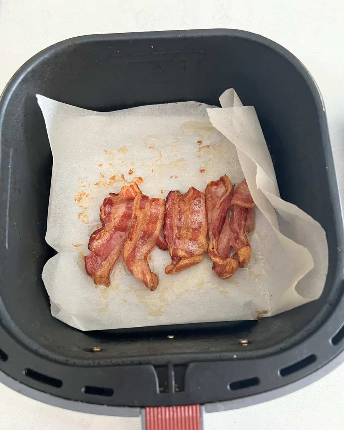 Crispy Air fried bacon on top of parchment paper in air fryer basket. 