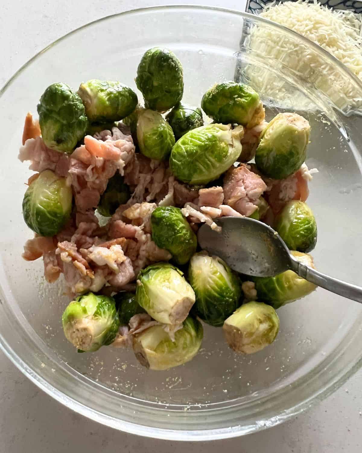 Brussel sprouts and bacon in a bowl mixed with olive oil and spices. 
