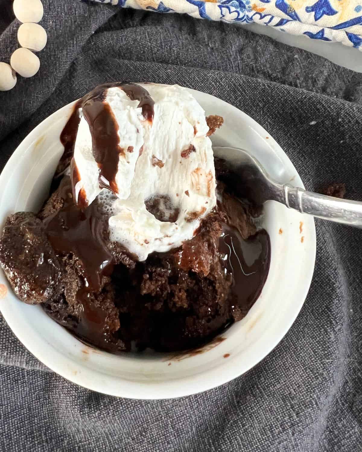 Single serving chocolate cake mix recipe in a white ramekin topped with cool whip and chocolate sauce. 