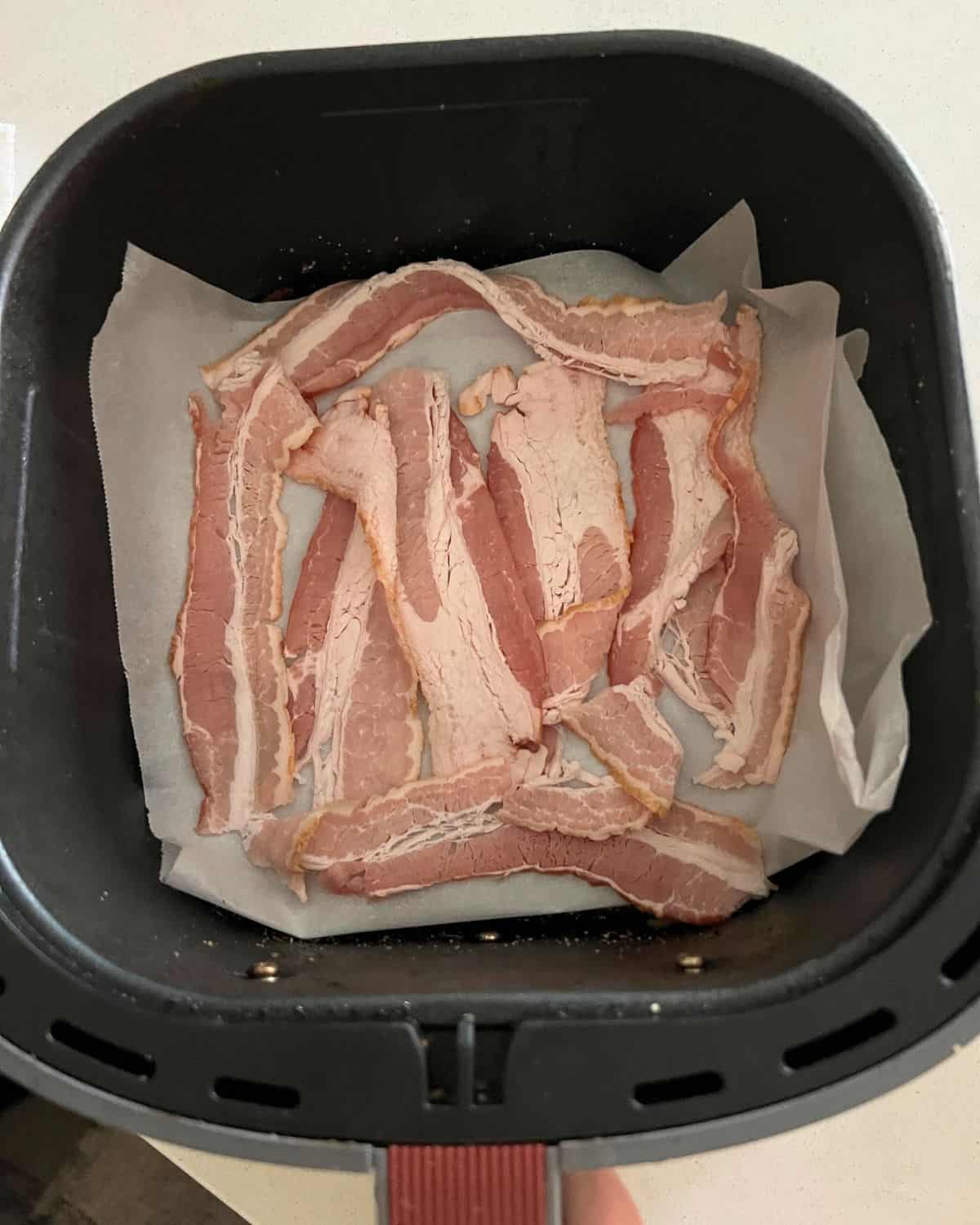 Air fryer bacon over parchment paper in air fryer basket. 
